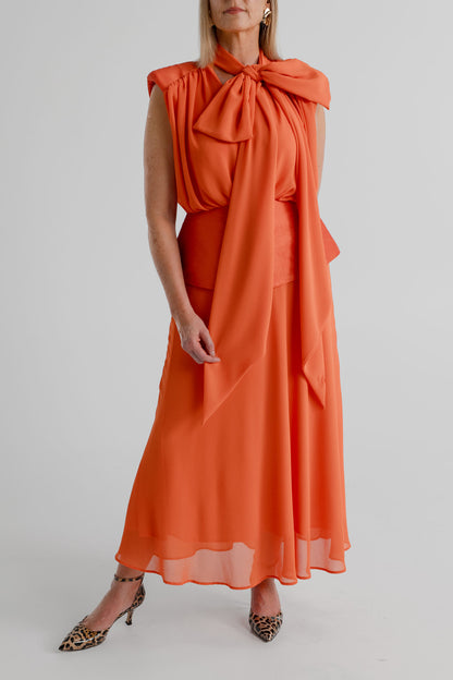 Front detail of the orange Strena Diana Midi Dress showing the gathered bodice, statement neck tie and structured peplum-style waist.
