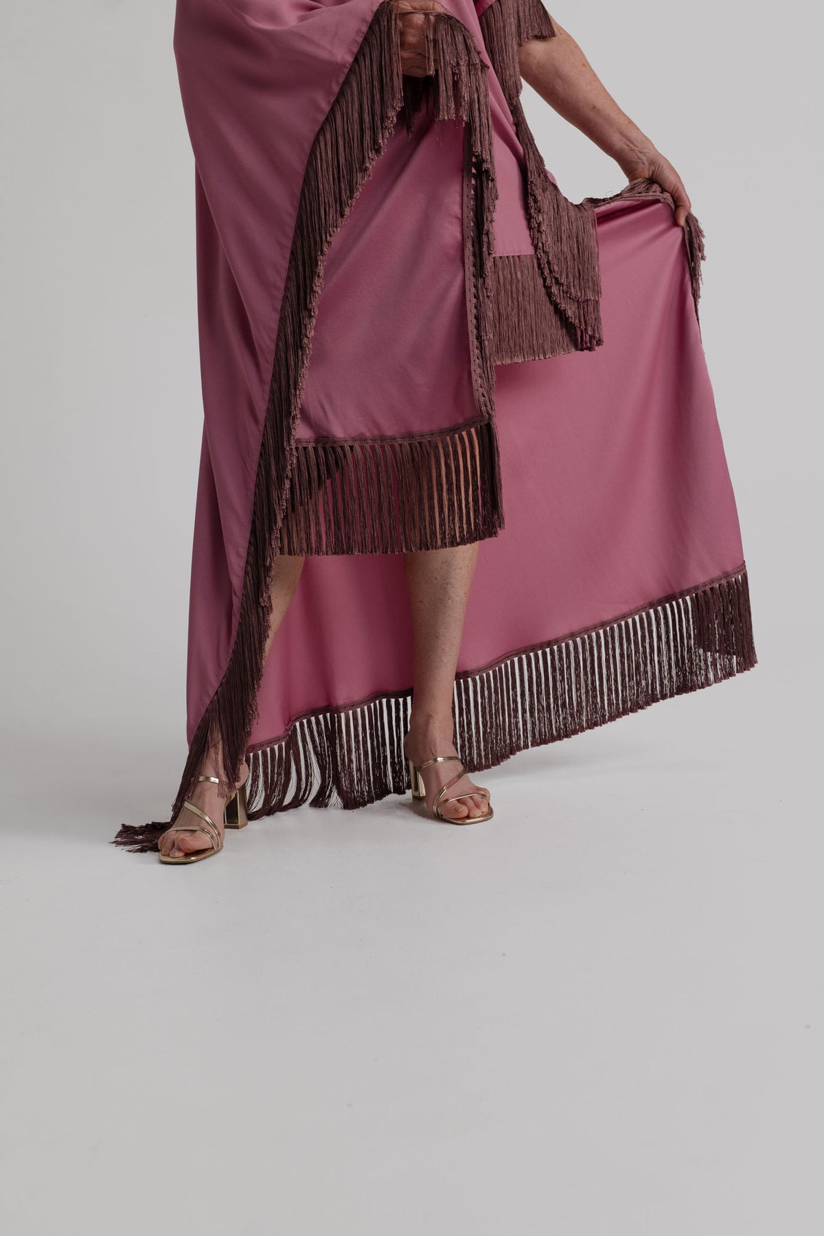 Close-up of the Taller Marmo Asymmetrical Fringed Satin Kaftan showing the dusty pink satin fabric, asymmetric drape and contrasting dark fringe trim.
