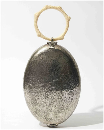 The Hold Capacity for Presence silver oval bag with textured metallic finish and ivory sculptural ring handle, front view. 
