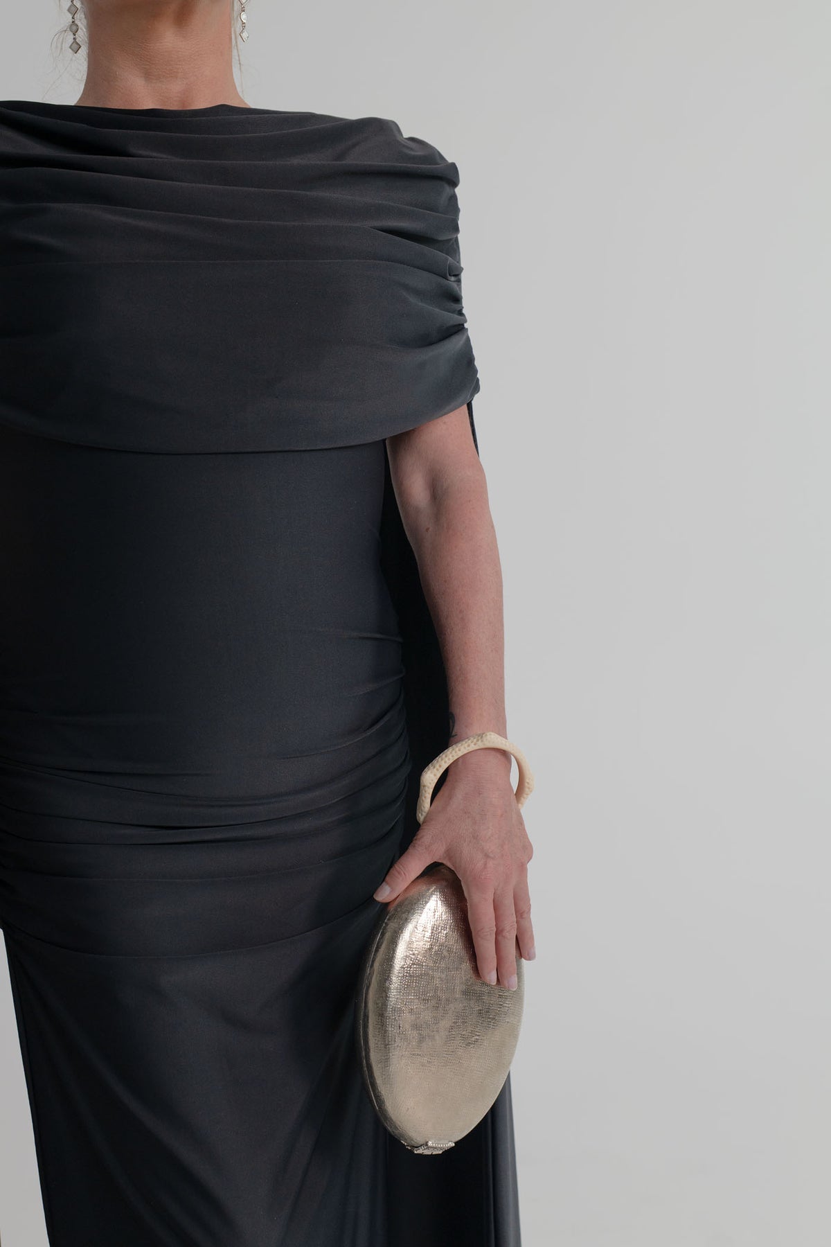 The Hold Capacity for Presence silver metallic bag with ivory sculptural ring handle, styled with the Mossman Reign black draped midi dress.
