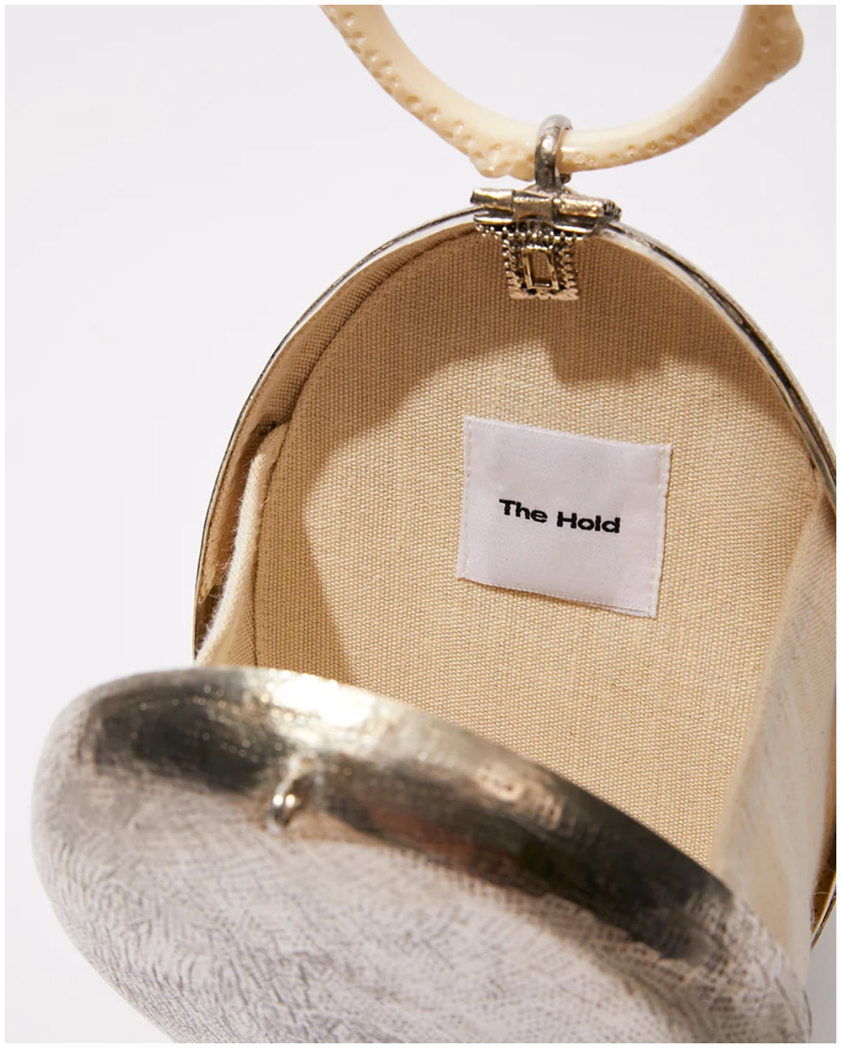 Open view of The Hold Capacity for Presence silver bag showing the light fabric interior and sculptural ivory ring handle. 
