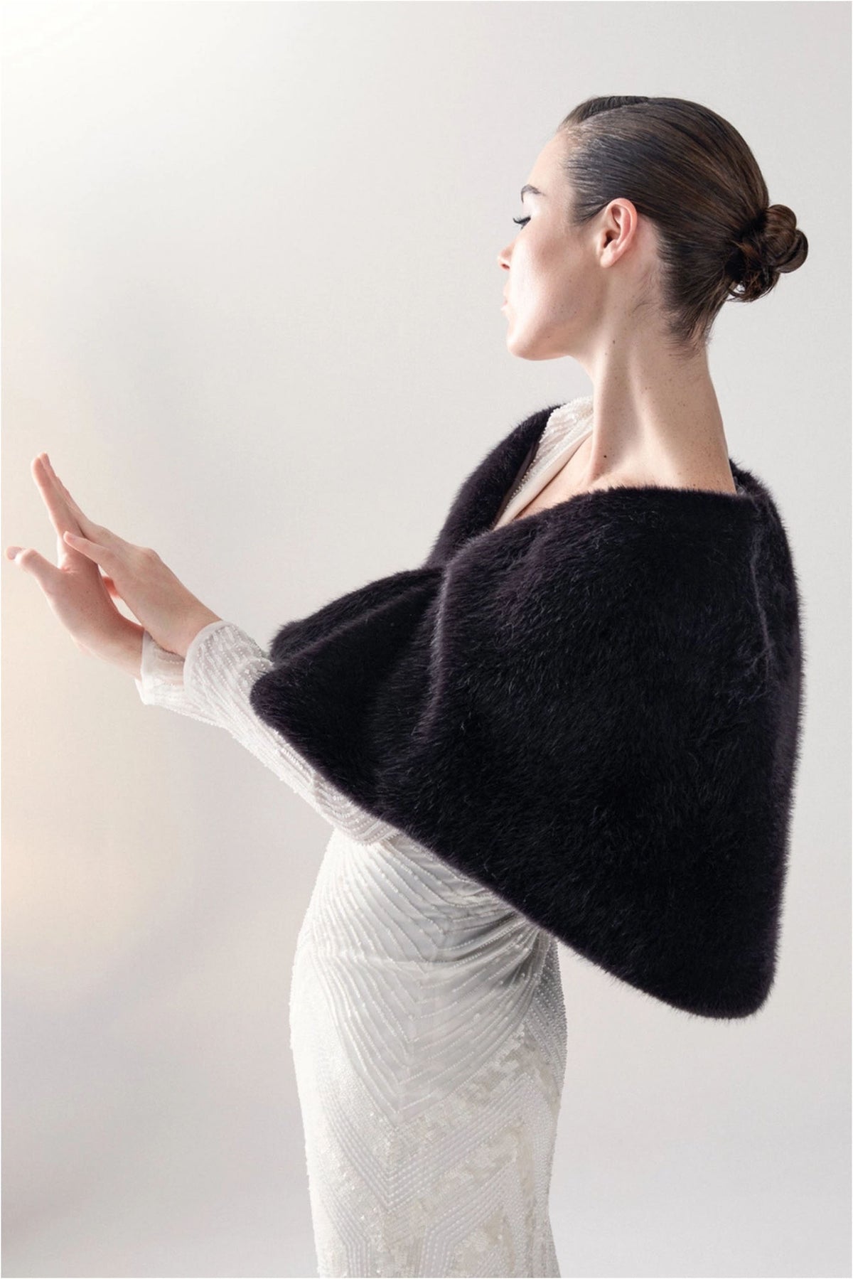 Side detail of Unreal Fur Yasmine Wrap in black faux fur showing the soft texture and draped cape silhouette. 
