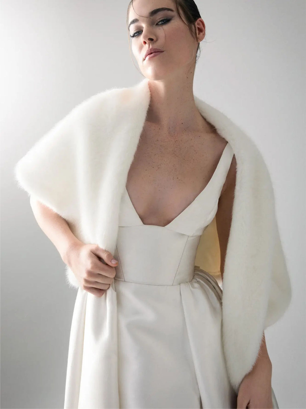 Editorial close-up of Unreal Fur Yasmine Wrap in white faux fur draped over the shoulders with a white gown. 
