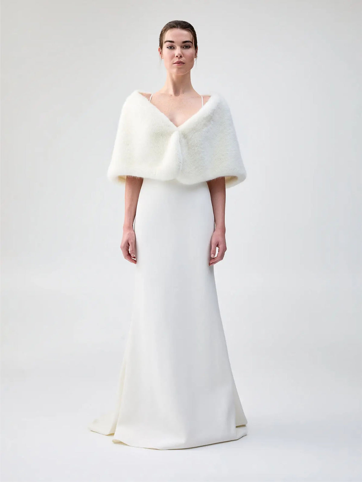 Front view of Unreal Fur Yasmine Wrap in white faux fur styled over a white gown. 

