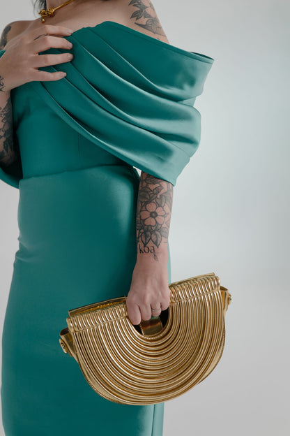 Close-up of the Verano Hill Amara gold ribbed semicircle handbag styled against the sculptural draped neckline of the Eliya the Label Vera teal dress.

