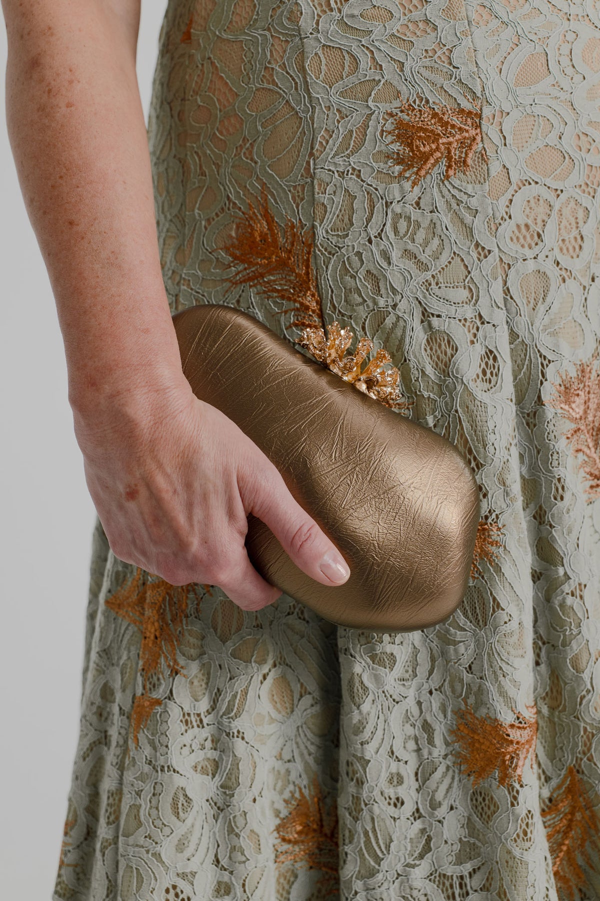 Close-up of the Verano Hill Coraline Sculpted clutch in metallic gold, styled with the sage lace IQ Collection Rose Maxi.
