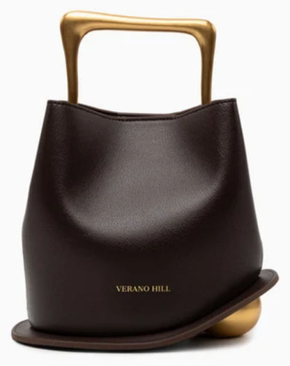 Verano Hill Vienna dark brown handbag with sculptural gold-tone top handle and curved base detail, front view. 
